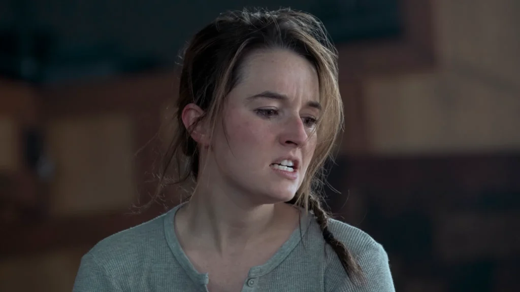 Abby com expressão tensa e emocional em cena de The Last of Us, usando uma camisa cinza e cabelo preso em trança