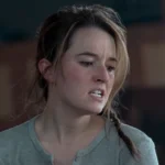 Abby com expressão tensa e emocional em cena de The Last of Us, usando uma camisa cinza e cabelo preso em trança
